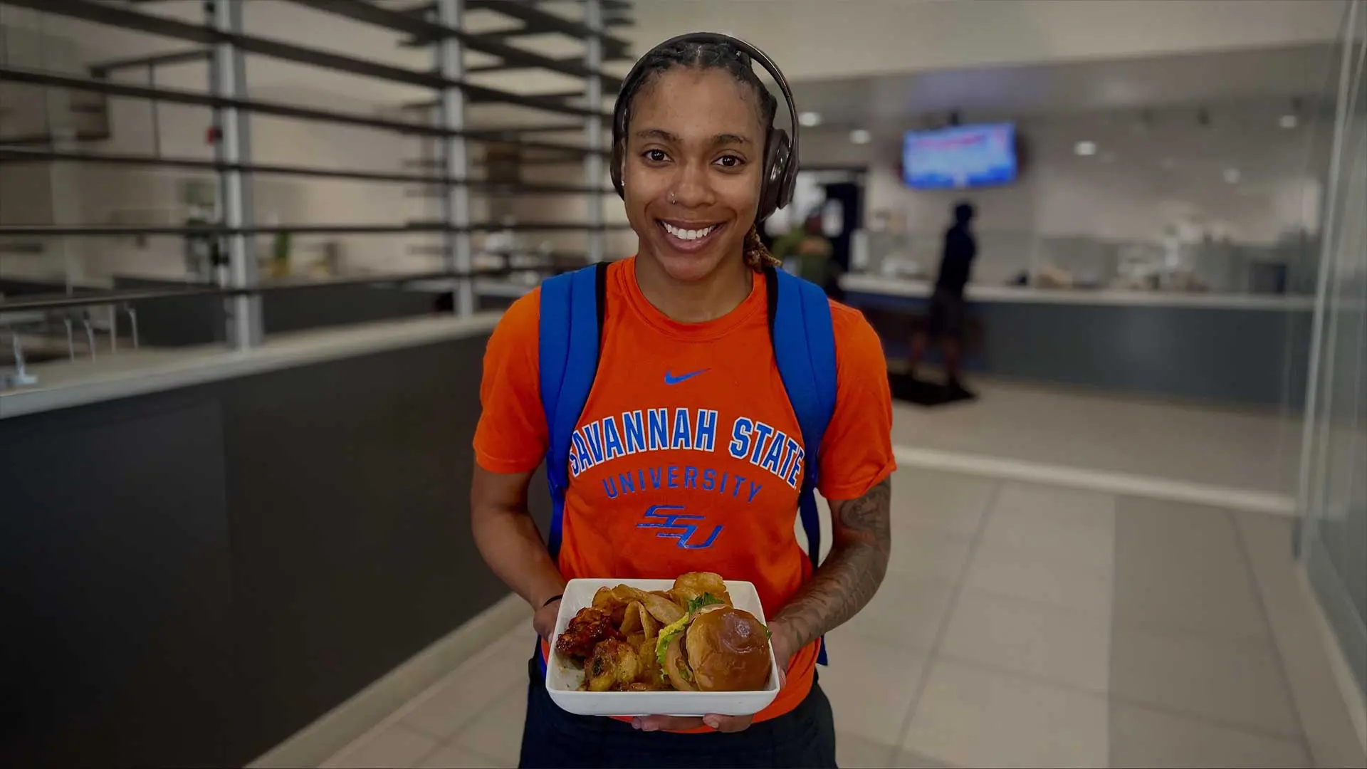 Student smiling while holding wings and sliders