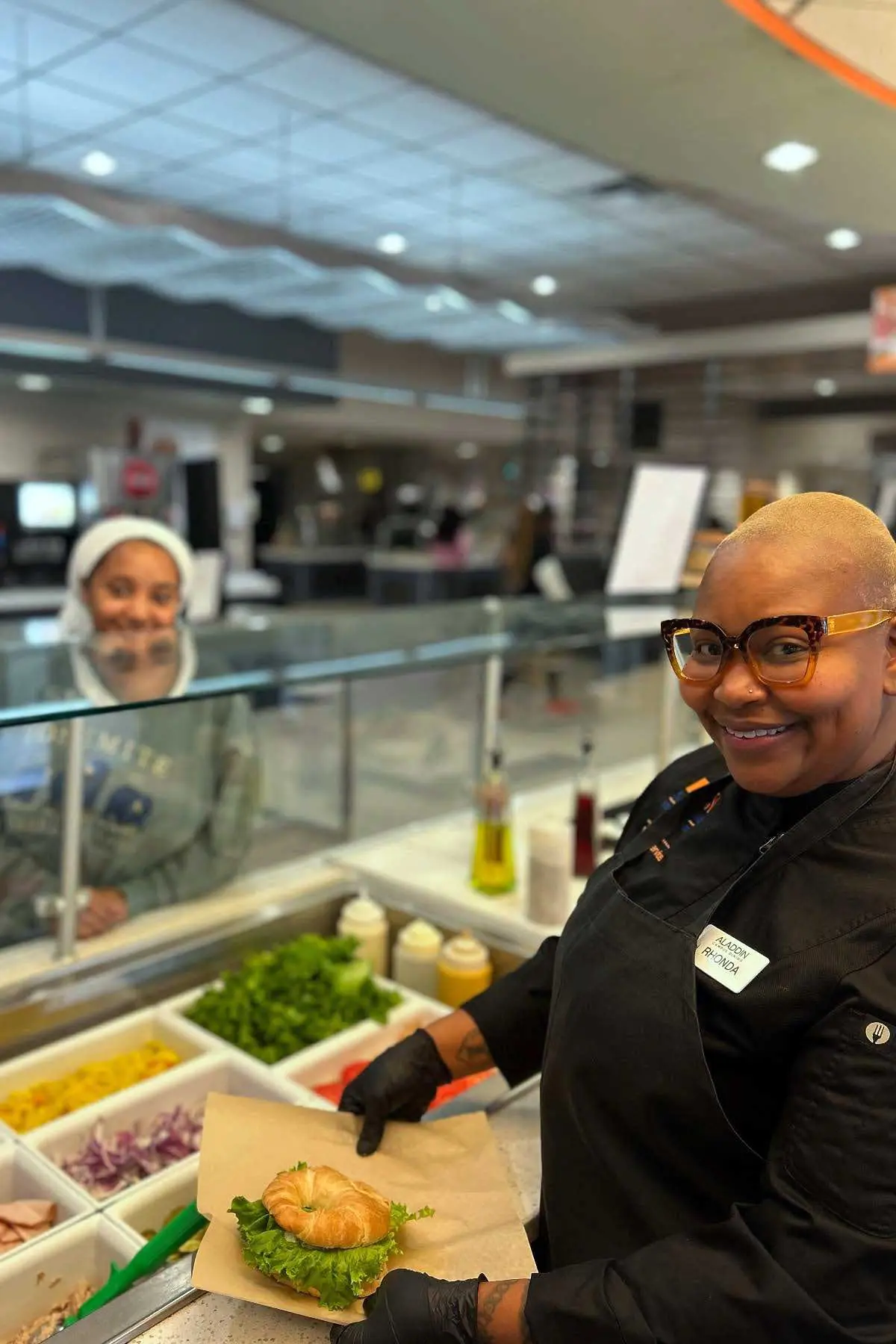 Working smiling with student while making a sandwich